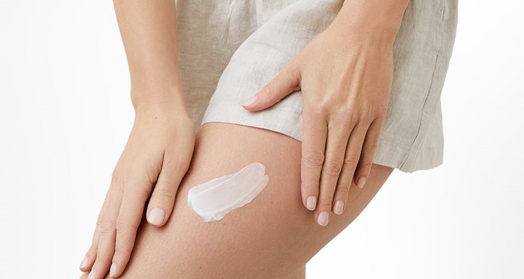 A closeup view of a model wearing light coloured shorts and with a cream product smudged against their left leg.