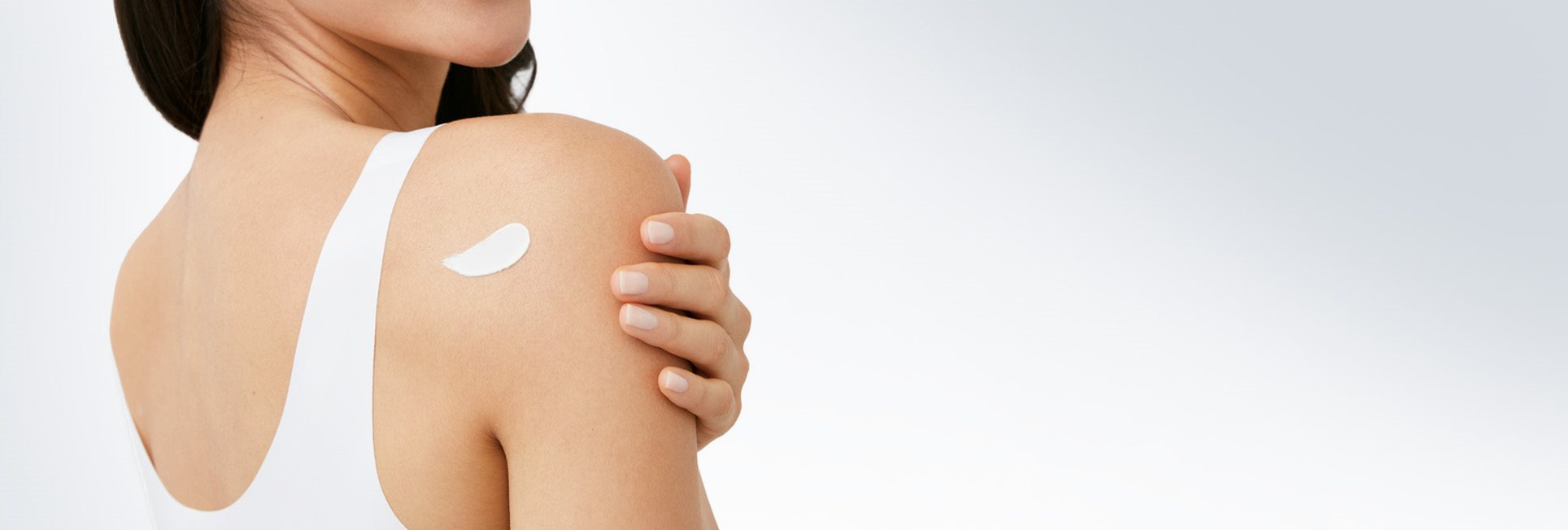 Femme mannequin vue de dos, avec une touche de produit en crème derrière son épaule droite.