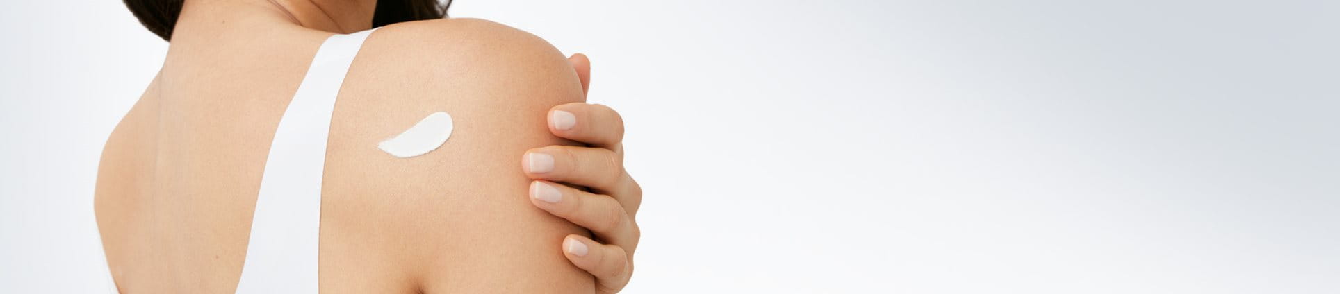 Femme mannequin vue de dos, avec une touche de produit en crème derrière son épaule droite.