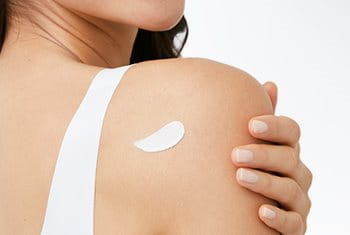 The back view of a model with a cream product smudged against the back of their right shoulder.