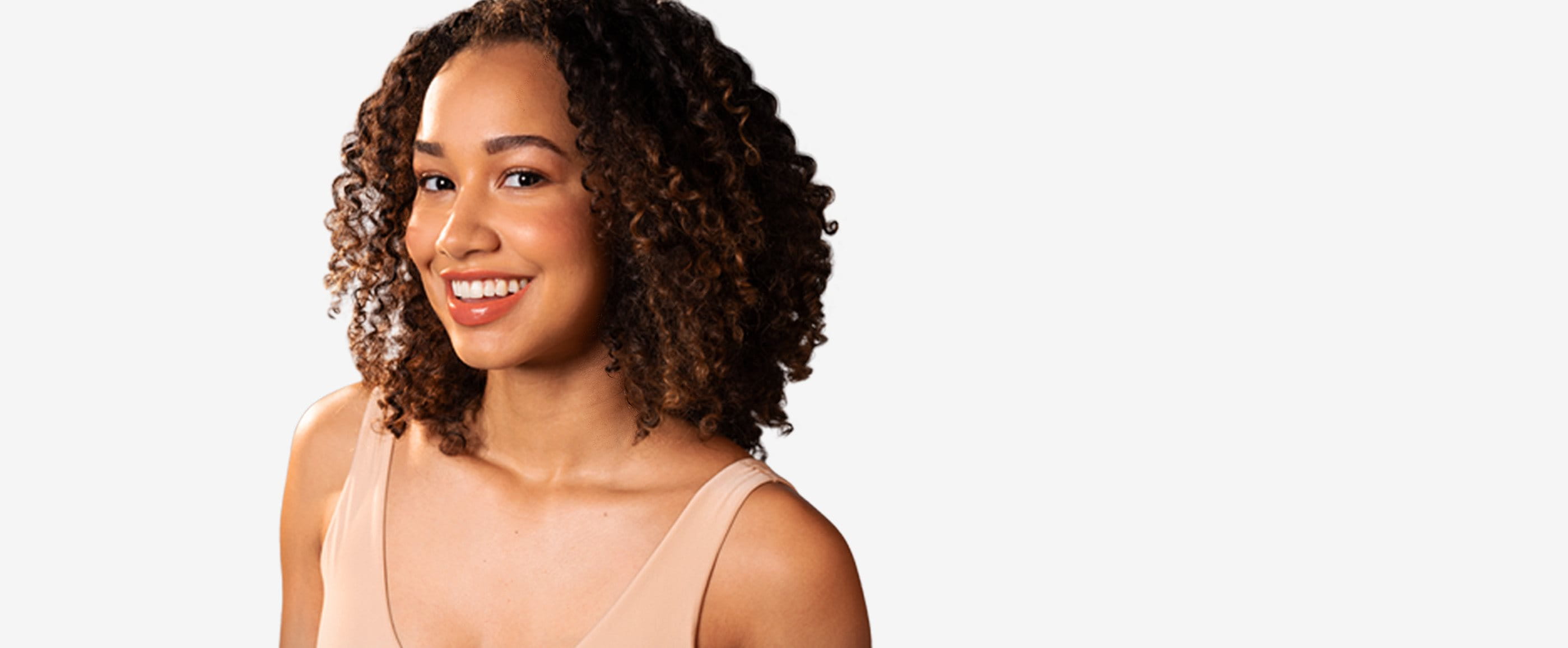 View of a person with brown curly hair smiling against a white background.