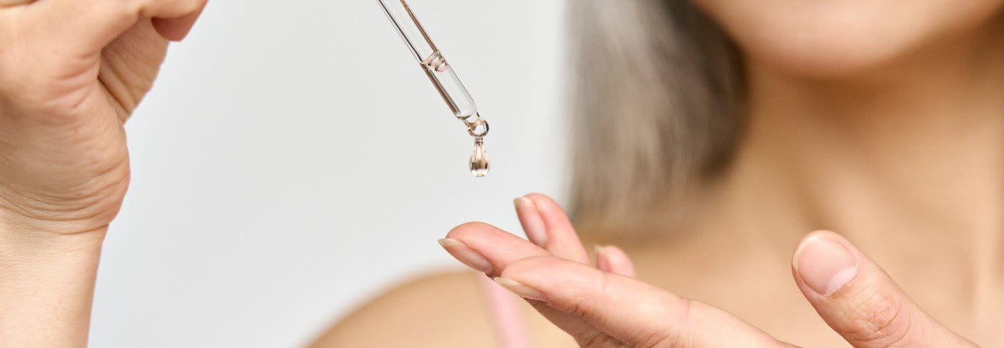 Gros plan sur une femme qui verse du sérum sur sa main.