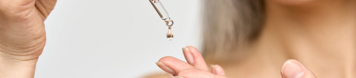 Gros plan sur une femme qui verse du sérum sur sa main.