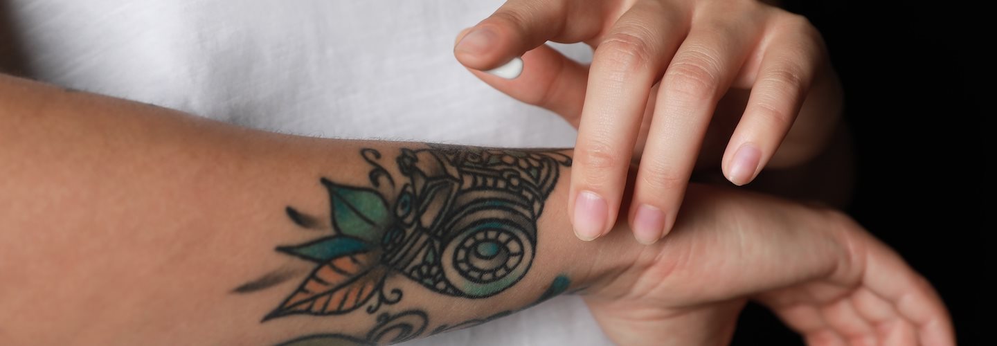 Frau cremt Tattoo am Arm mit Sonnencreme ein