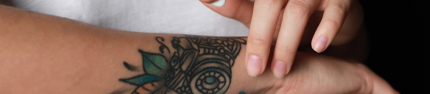 Frau cremt Tattoo am Arm mit Sonnencreme ein