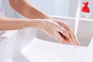 Frau, die ihre eingeseiften Hände unter fließendem Wasser wäscht