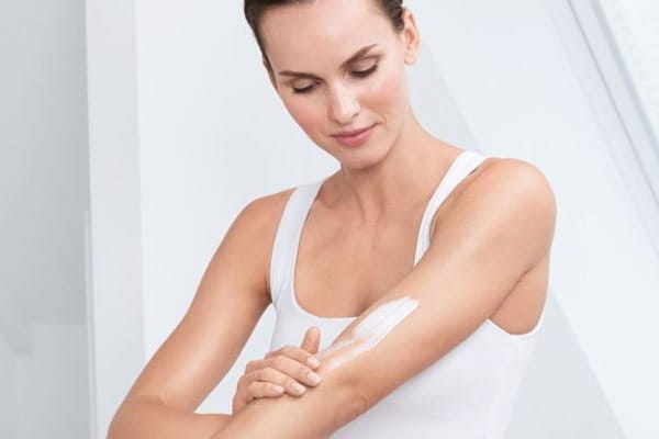 Frau mit Keratosis pilaris cremt sich den Arm ein