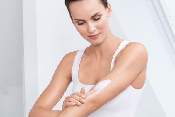 Frau mit Keratosis pilaris cremt sich den Arm ein