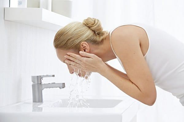 Frau wäscht sich das Gesicht am Waschbecken