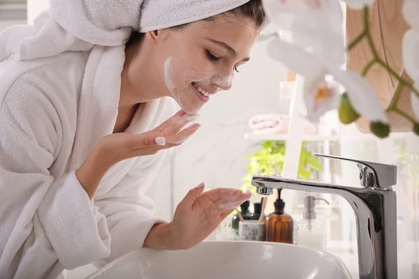 Frau am Waschbecken trägt Gesichtsreinigung auf