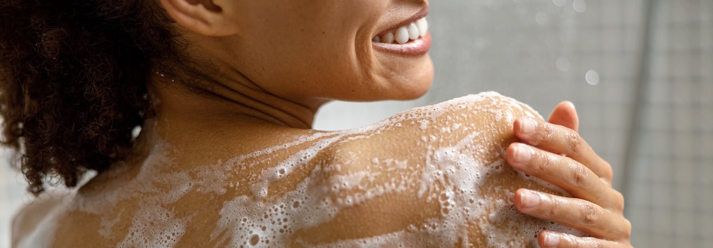 Frau unter der Dusche reinigt Haut auf den Schultern und am Rücken