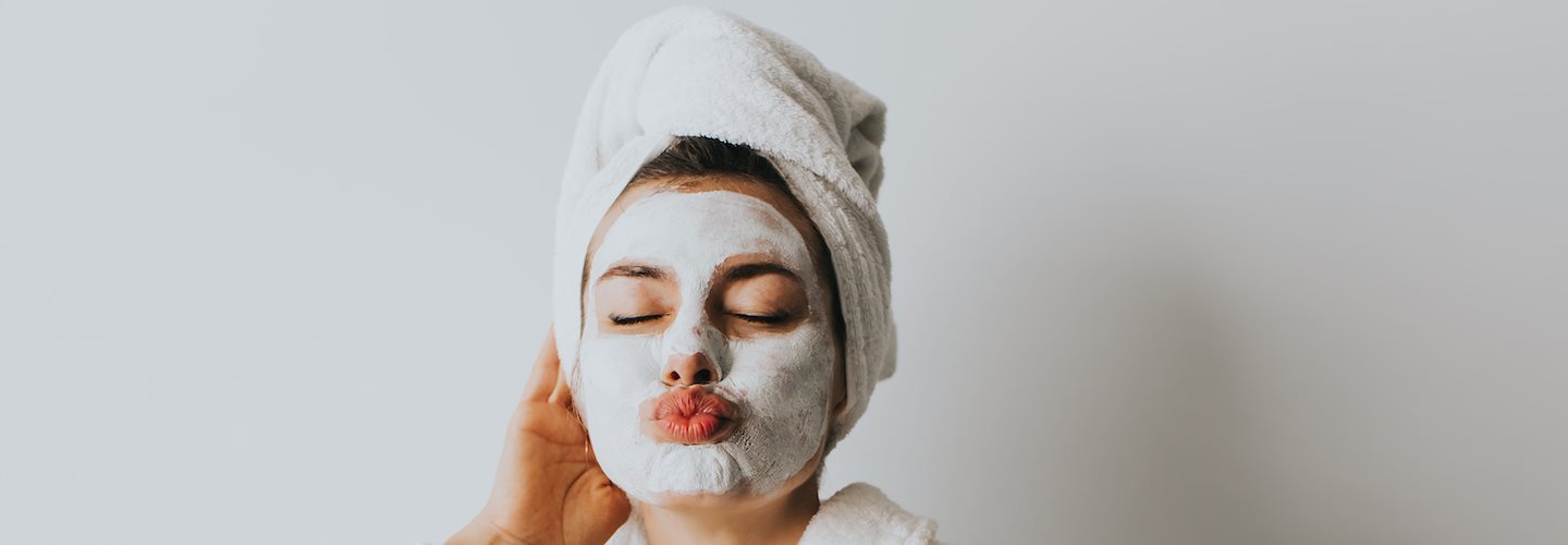 Entspannte Frau im Bademantel mit Gesichtsmaske und Getränk