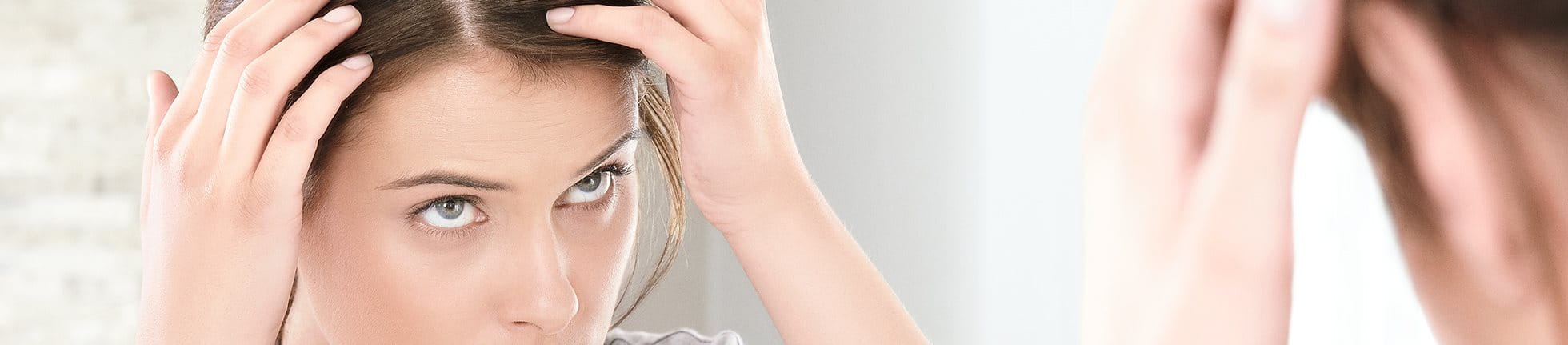 Frau untersucht ihren Scheitel im Spiegel