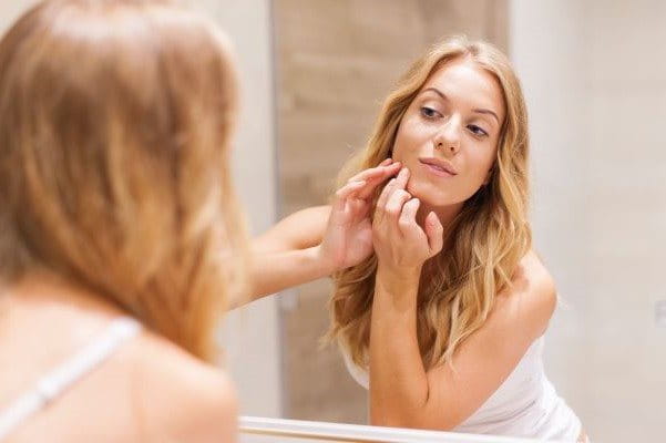 Frau mit Spätakne (akne tarda) schaut sich im Spiegel an