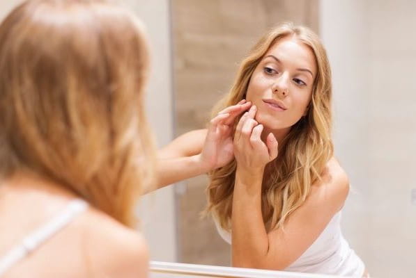 Frau mit Spätakne (akne tarda) schaut sich im Spiegel an