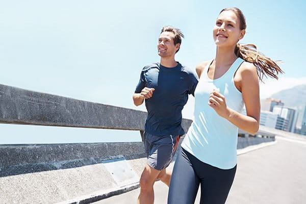 Mann und Frau joggen unter blauem Himmel. Sie tragen Funktionskleidung, was dabei hilft, Rückenakne vorzubeugen.