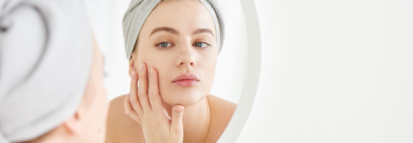 Junge Frau vor dem Spiegel berührt mit der Hand ihre Wange