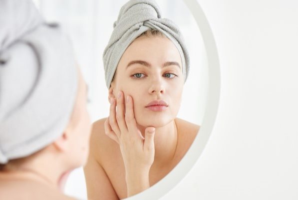 Junge Frau vor dem Spiegel berührt mit der Hand ihre Wange