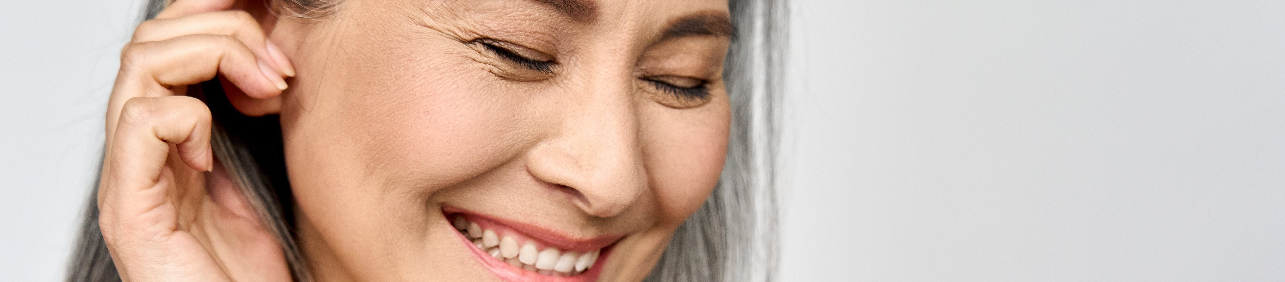 Lachende, ältere Frau streicht sich Haare aus dem Gesicht.