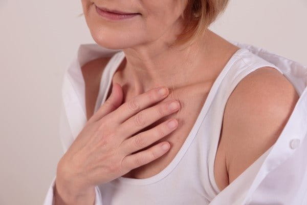 Frau legt eine Hand auf das Dekolleté