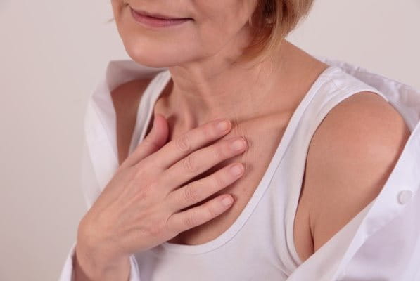 Frau legt eine Hand auf das Dekolleté