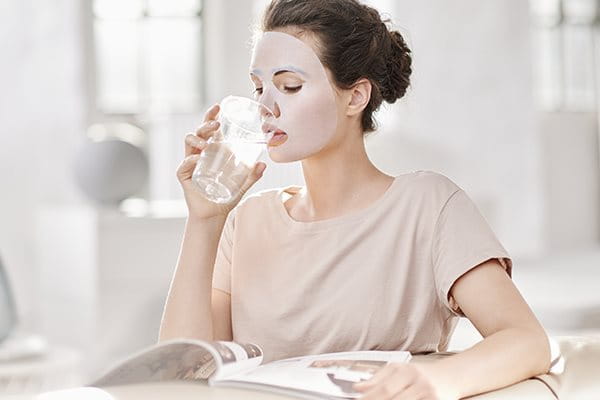 Frau mit Tuchmaske trinkt ein Glas Wasser