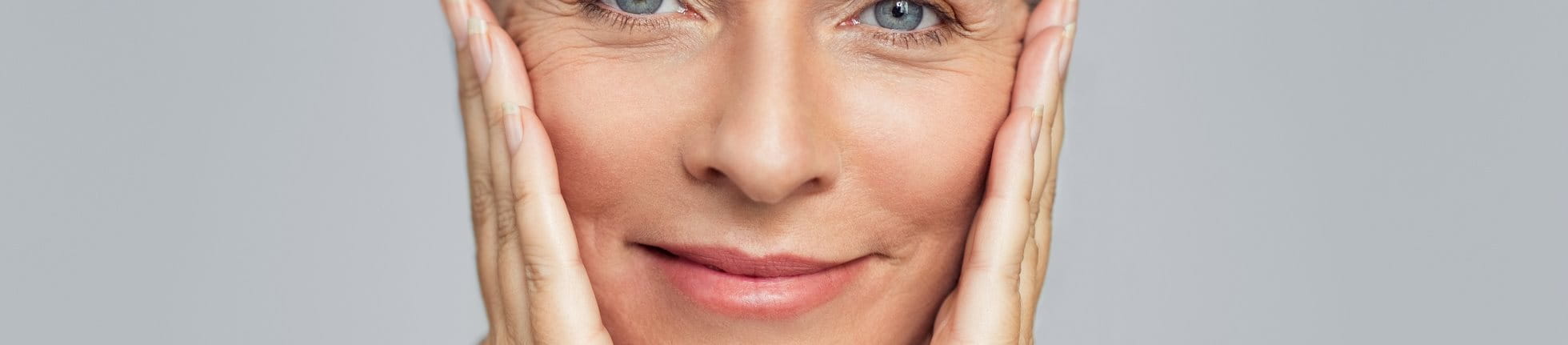 Frau mit Krähenfüßen hält sich die Hände an die Wangen