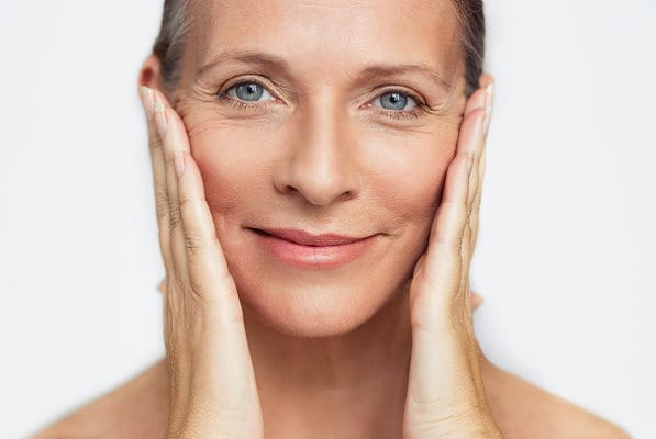 Ältere Frau mit Krähenfüßen hält sich die Hände an die Wangen