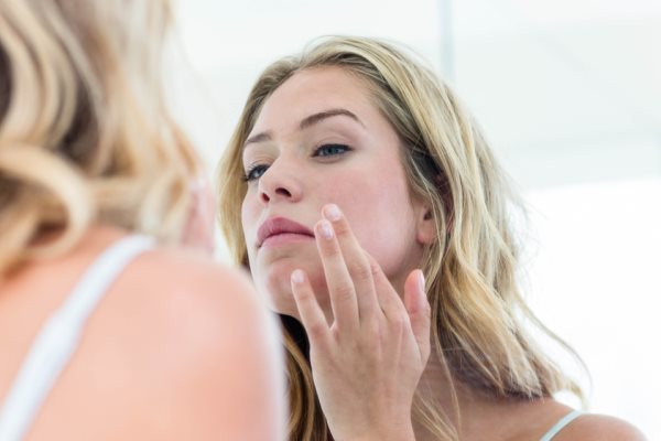 Frau guckt Haut im Spiegel an