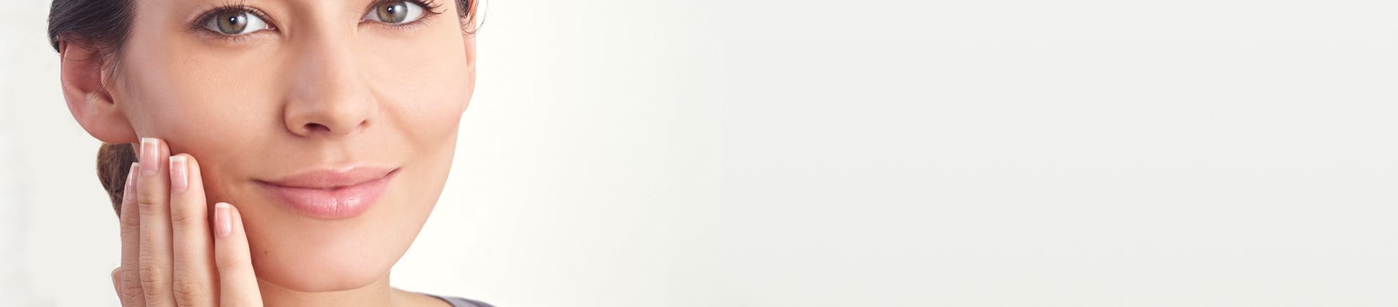 Woman with clear skin touching her face against a light background.