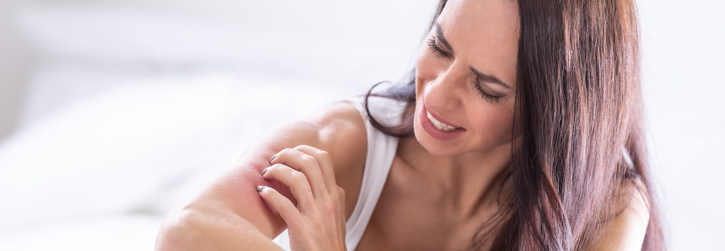 Frau im Bett kratzt sich am Arm