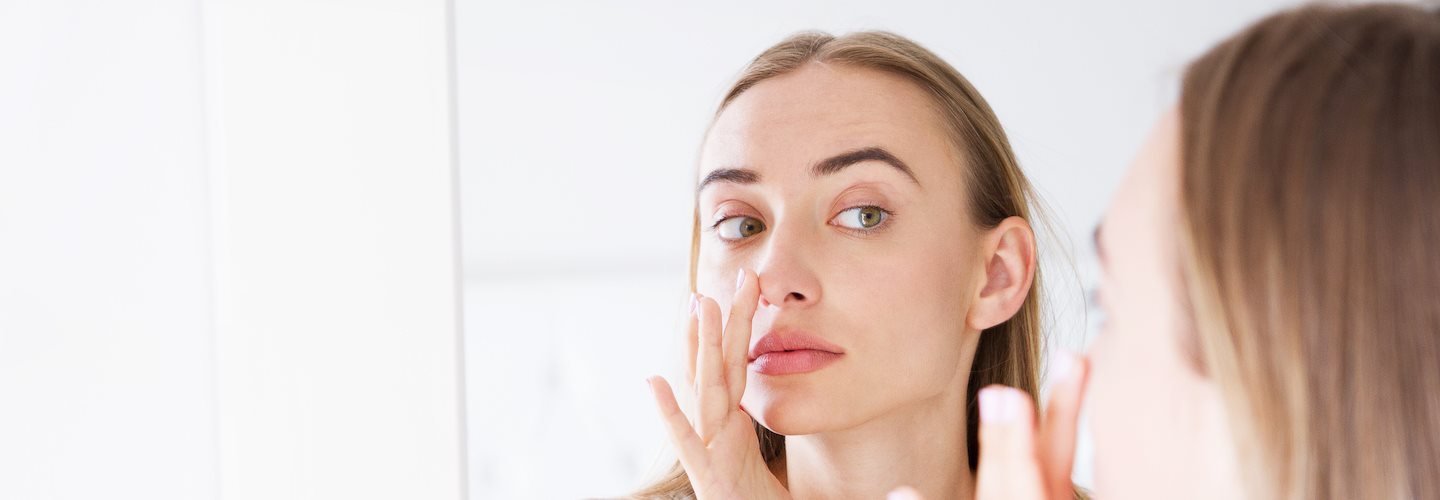 Frau betrachtet Rötung der Nase im Spiegel