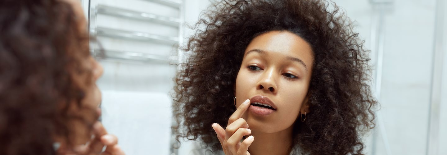 Frau im Spiegel streicht sich mit dem Finger über die Oberlippe