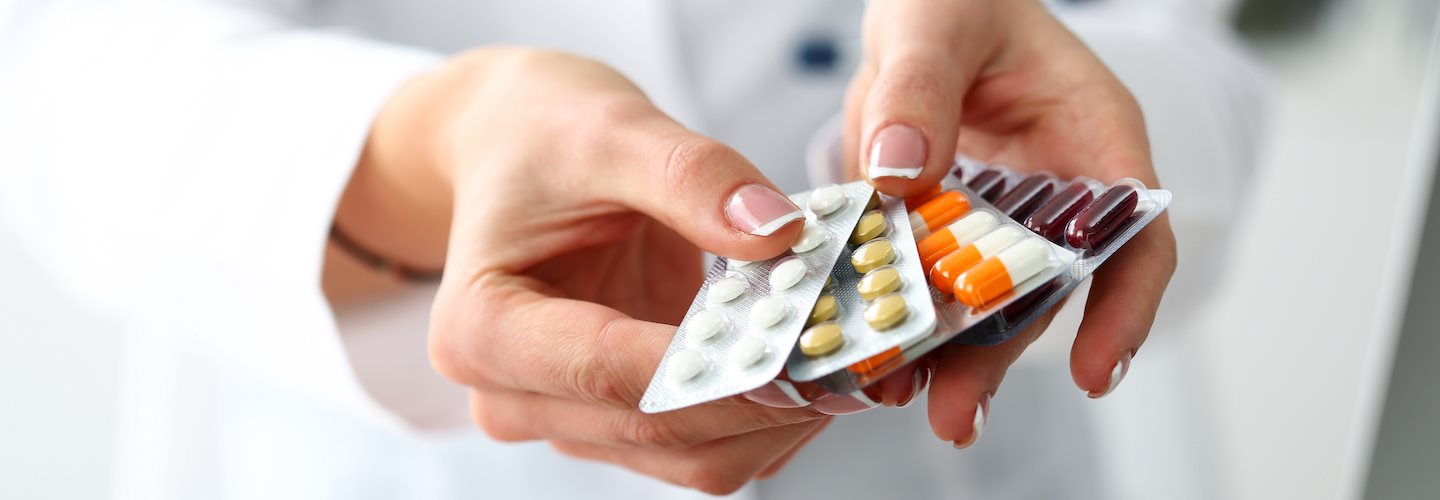 Zwei Hände reichen mehrere Medikamentepackungen in Richtung des Betrachters.
