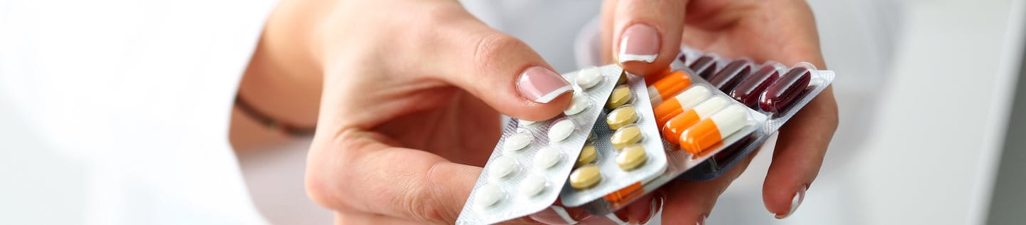 Zwei Hände reichen mehrere Medikamentepackungen in Richtung des Betrachters.