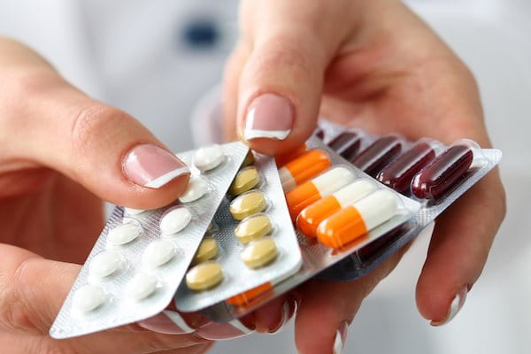 Zwei Hände reichen mehrere Medikamentepackungen in Richtung des Betrachters.