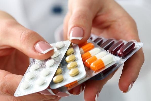 Zwei Hände reichen mehrere Medikamentepackungen in Richtung des Betrachters.