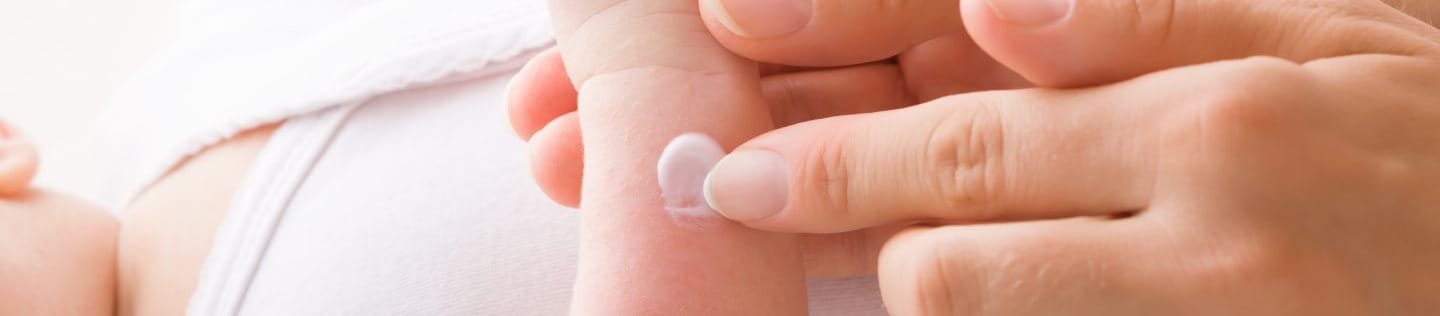 Mutter trägt Salbe auf den neugeborenen Arm auf