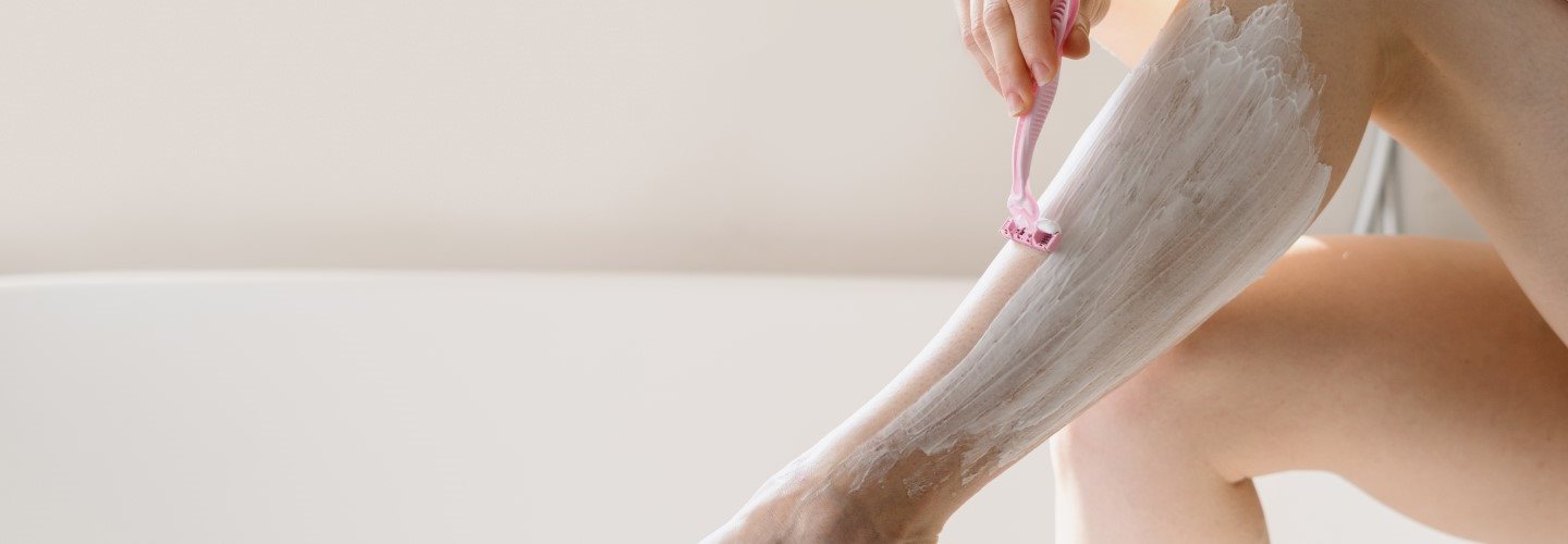 Bein einer Frau beim Rasieren, das auf einem Badewannenrand abgestützt wird.