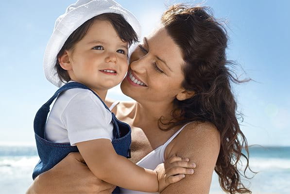Frau am Strand hält Kind im Arm