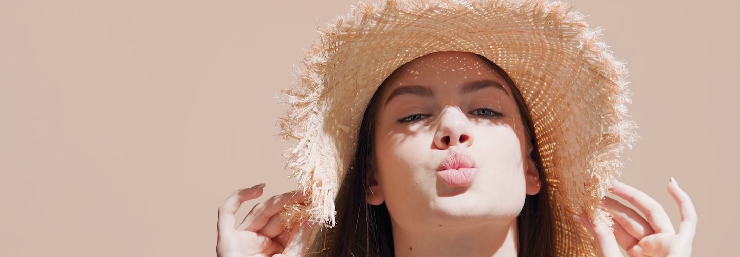 Dunkelhaarige Frau mit Strohhut auf dem Kopf, die die Lippen spitzt