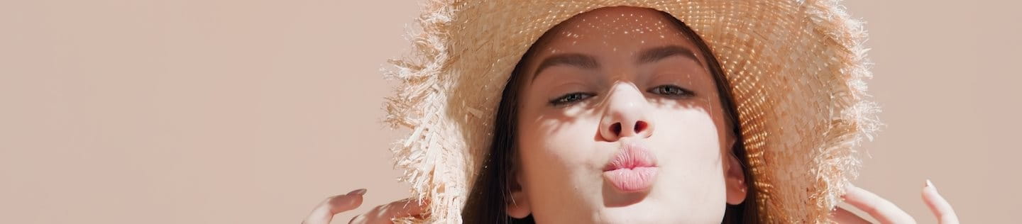 Dunkelhaarige Frau mit Strohhut auf dem Kopf, die die Lippen spitzt