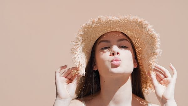 Dunkelhaarige Frau mit Strohhut auf dem Kopf, die die Lippen spitzt