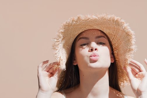 Dunkelhaarige Frau mit Strohhut auf dem Kopf, die die Lippen spitzt