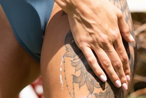 Frau cremt sich tätowierten Oberschenkel mit Sonnencreme ein