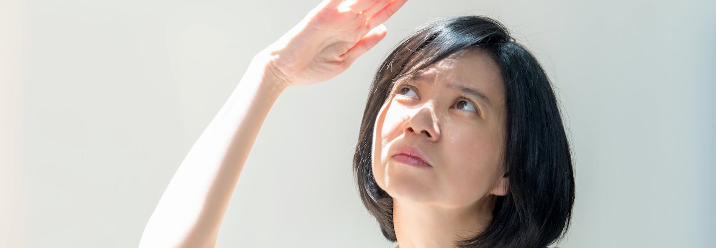 Eine Frau mit hellem Hauttyp hebt ihre Hand zum Schutz vor der Sonne über das Gesicht