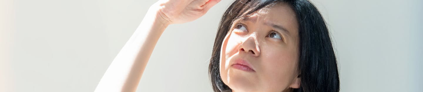 Eine Frau mit hellem Hauttyp hebt ihre Hand zum Schutz vor der Sonne über das Gesicht