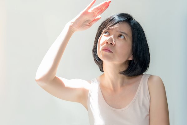 Eine Frau mit hellem Hauttyp hebt ihre Hand zum Schutz vor der Sonne über das Gesicht