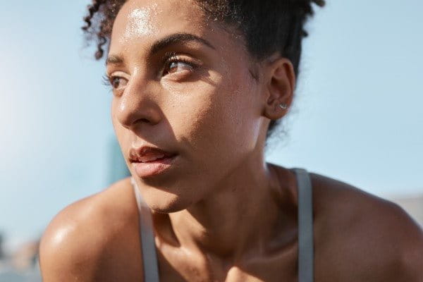 Junge Frau mit schweißbedecktem Gesicht, entspannt nach einem intensiven Training in der Sonne.