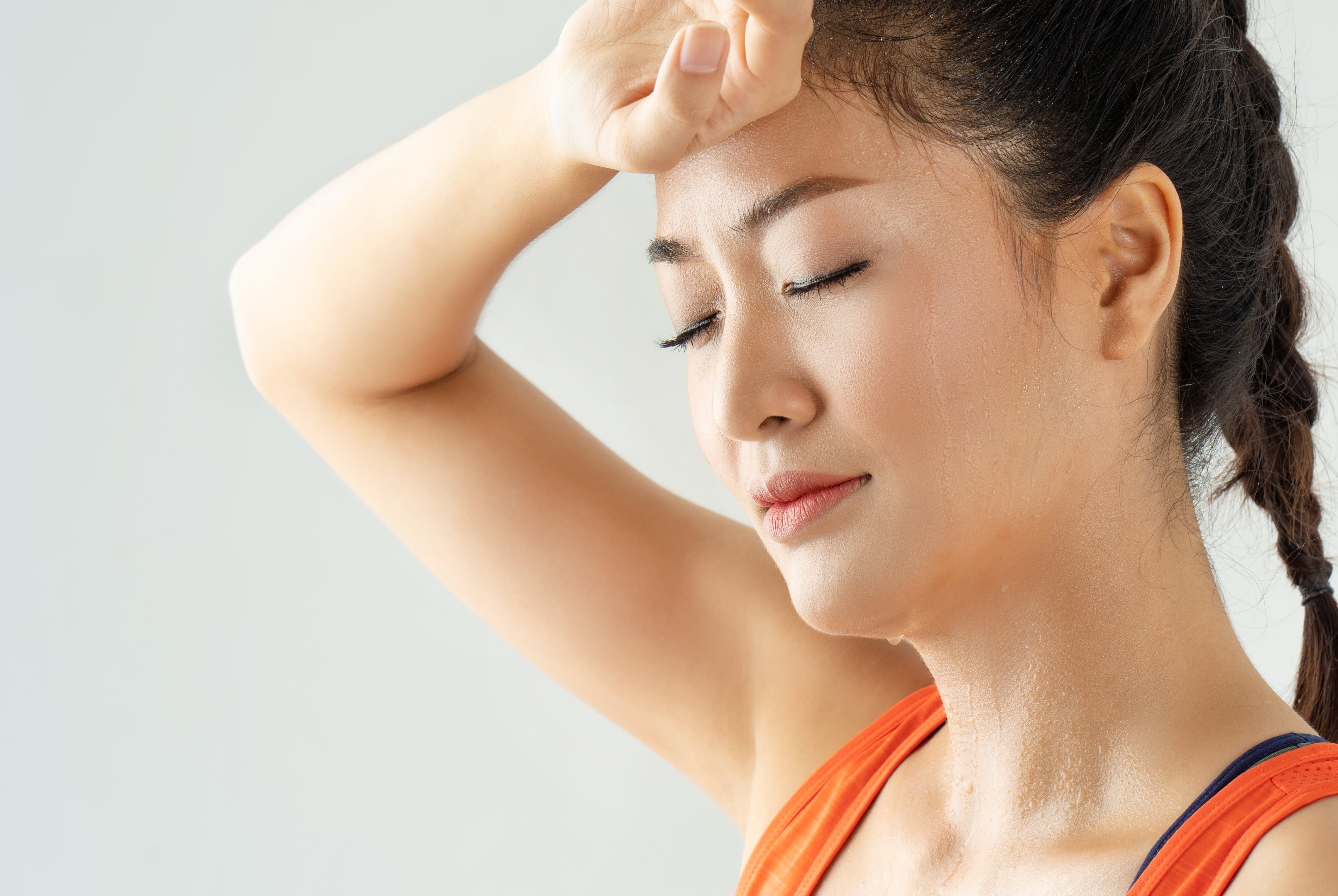 Frau mit geschlossenen Augen wischt sich den Schweiß von der Stirn nach dem Training.